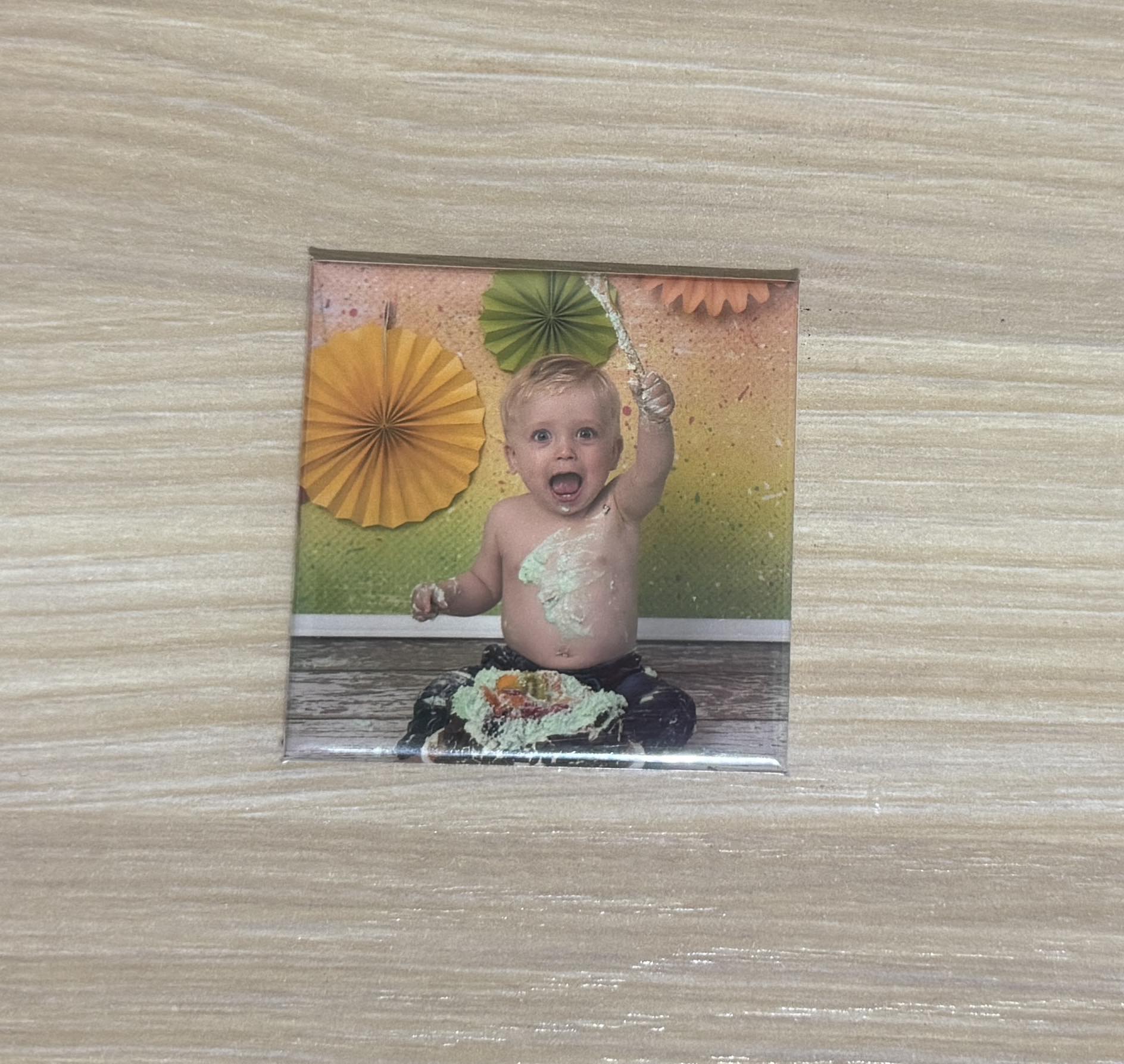 Photo magnet of a baby boy celebrating a cake smash with colorful green and orange decorations.