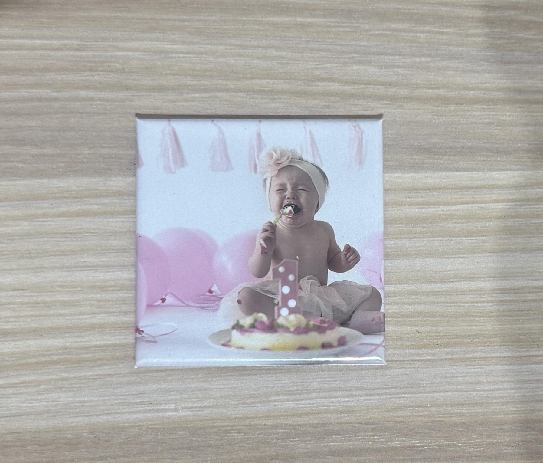 Photo magnet of a baby girl crying during her pink-themed cake smash first birthday celebration.